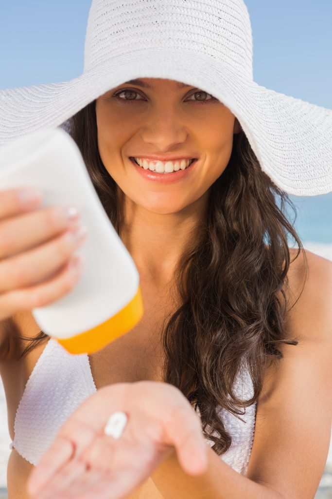 alt=" uśmiechnięta kobieta w kapeluszu z kremem UVA/UVB fotoprotekcja"